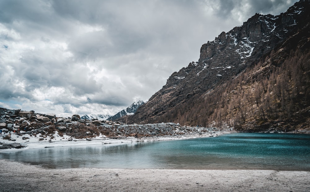 Montañas marrones y blancas junto al cuerpo de agua bajo nubes blancas durante el día