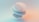 A minimalist 3D abstract composition featuring layered, translucent geometric shapes with smooth surfaces. The elements are primarily spherical and elliptical, with subtle shading and gradients creating a sense of depth and dimension. The backdrop has a soft, diffused gradient of peach and teal colors, enhancing the ethereal quality.