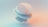 A minimalist 3D abstract composition featuring layered, translucent geometric shapes with smooth surfaces. The elements are primarily spherical and elliptical, with subtle shading and gradients creating a sense of depth and dimension. The backdrop has a soft, diffused gradient of peach and teal colors, enhancing the ethereal quality.