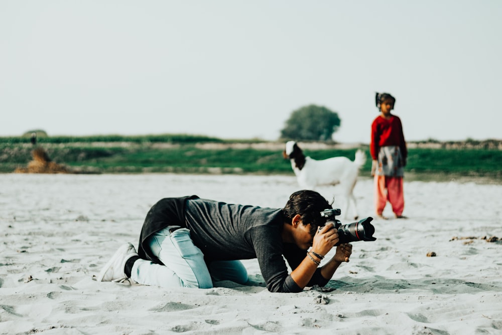 Un uomo sdraiato nella sabbia con una macchina fotografica