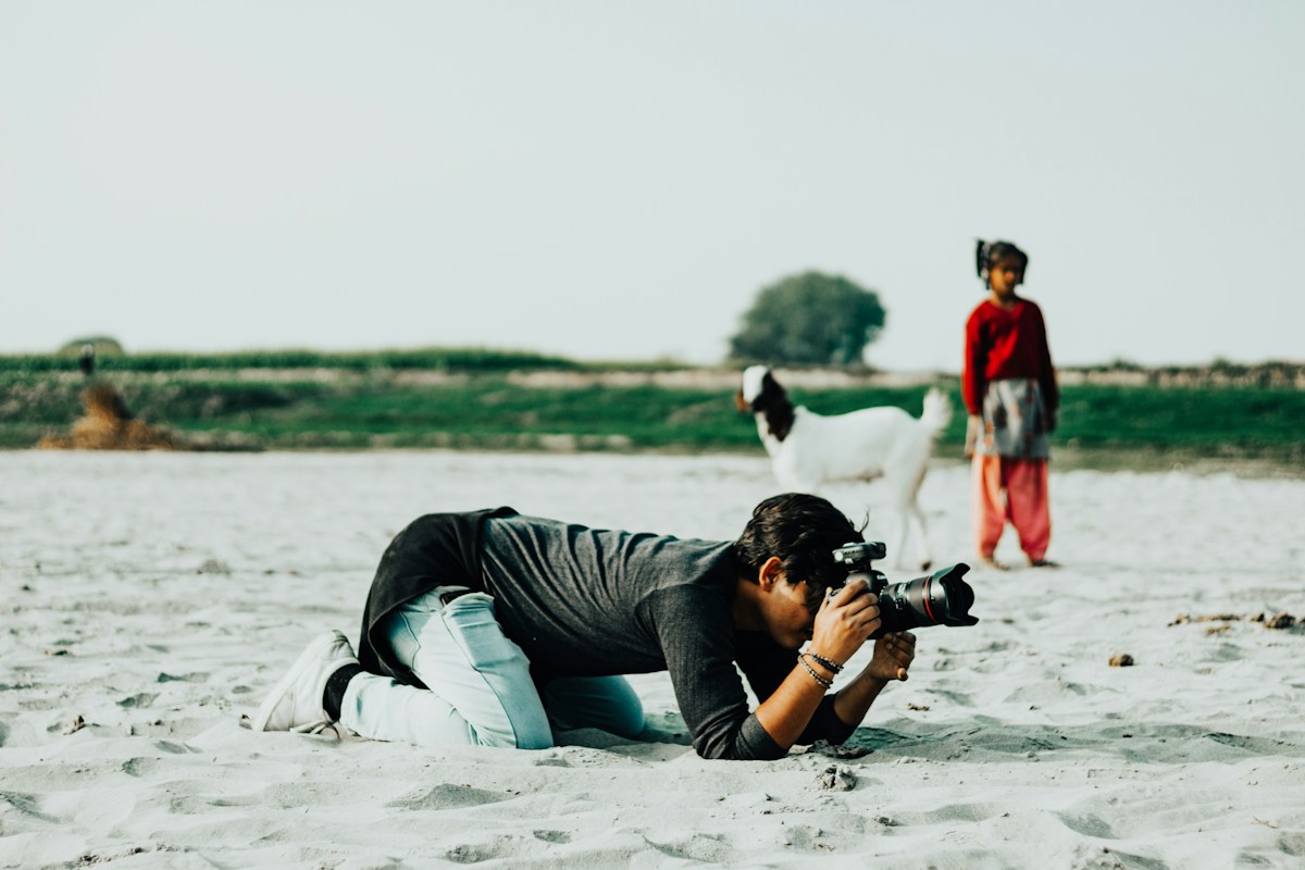 A volunteer at Matthews UMC Walk Through Bethlehem captures event moments with a camera while lying on the sand.