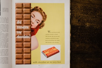 A vintage advertisement featuring a woman in red gloves peeking from behind a large Nestlé's chocolate bar, with the text 'did someone say chocolate!' on the chocolate. The background is yellow with descriptive text about the chocolate's creamy flavor and smoothness. A smaller image of a Nestlé's chocolate package is displayed at the bottom.