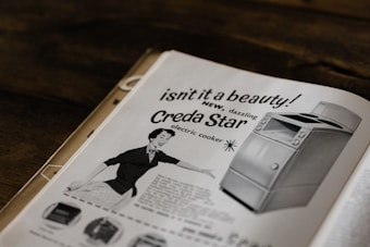 A vintage advertisement featuring a smiling woman presenting a Creda Star electric cooker. The ad uses bold text and illustrations to highlight the modern and appealing design of the appliance.