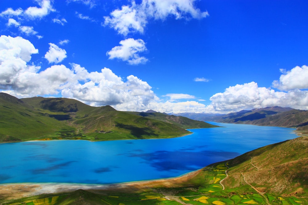 green mountain beside blue body of water under blue sky and white clouds during daytime