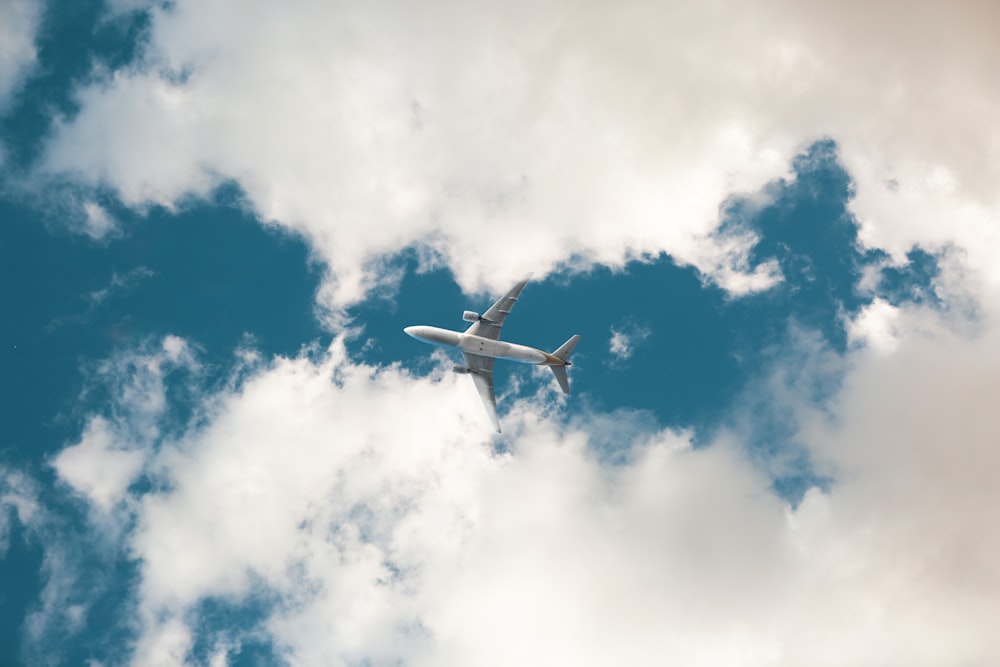 white airplane flying under blue sky during daytime