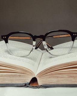 Close-up of a pair of glasses resting on an open book, symbolizing clarity and focus