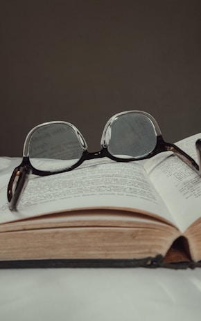 An open textbook with notes and a pair of glasses resting on top.