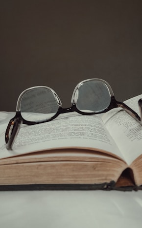Close-up of an open paperback book with a pair of glasses resting on the pages.