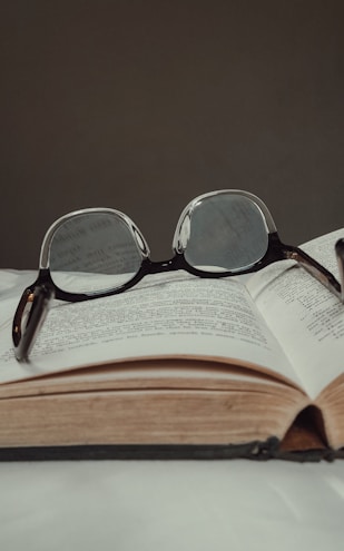 An open textbook with notes and a pair of glasses resting on top.