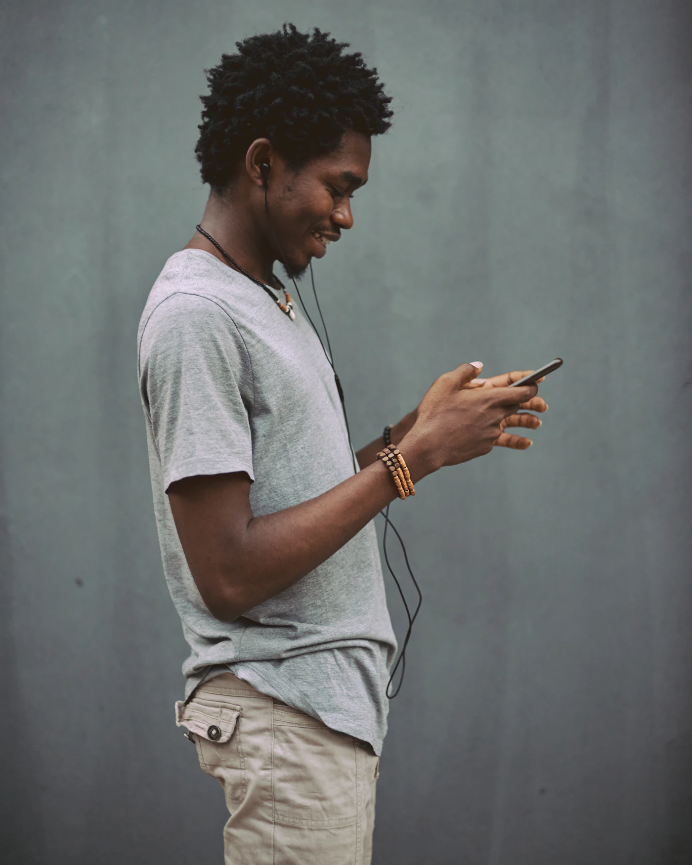 A young man smiling while using his smartphone with earphones