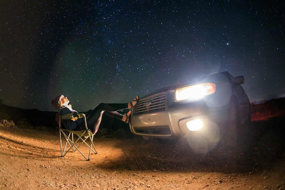 man and woman sitting on camping chairs beside black suv during night time