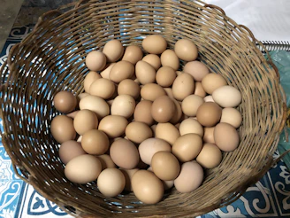 Close-up of a basket filled with freshly gathered brown and white eggs on a rustic wooden table.