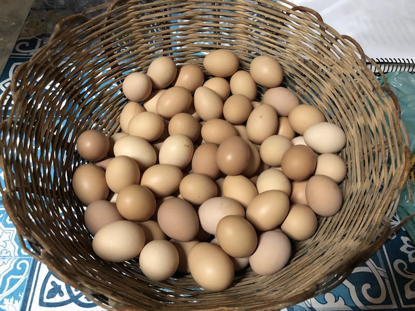 A rustic basket filled with fresh eggs and seasonal vegetables on a wooden table.