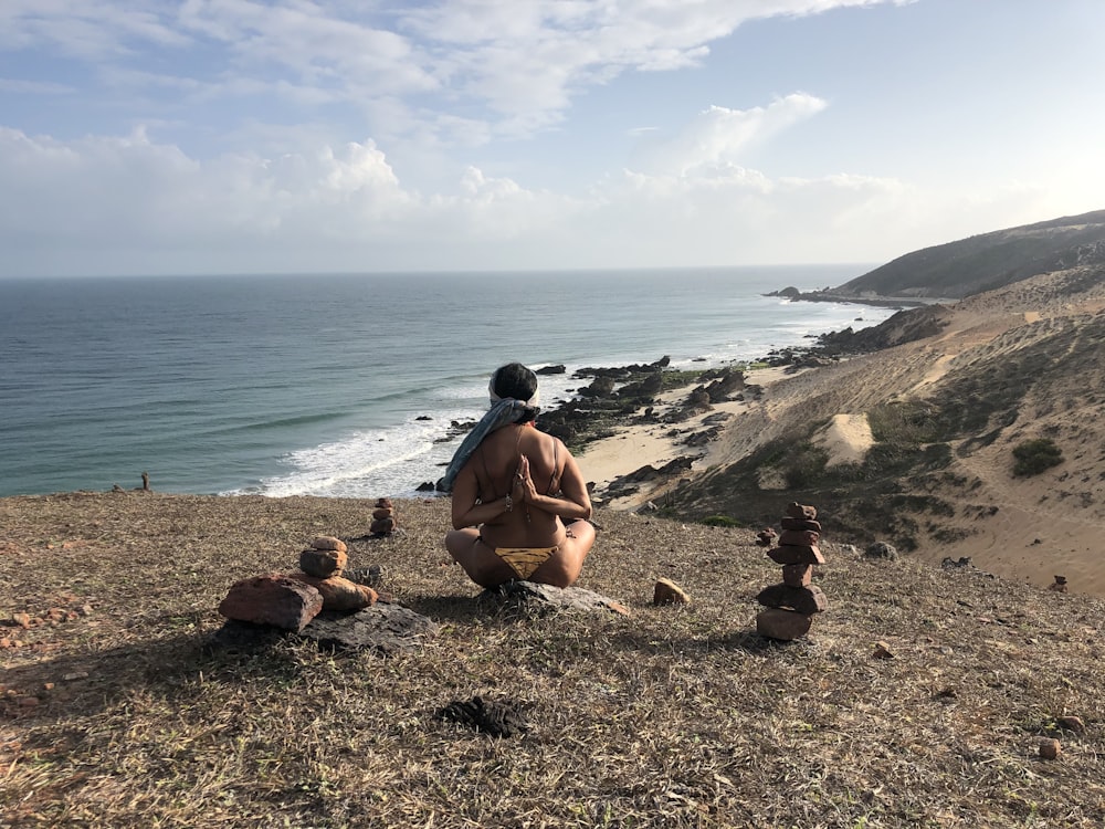 man in black shorts sitting on brown rock near body of water during daytime