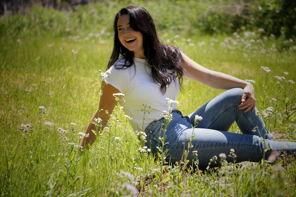 woman in white shirt and blue denim jeans sitting on green grass field during daytime
