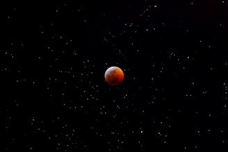 An astrophotography shot of a lunar eclipse with the moon glowing in deep red hues.
