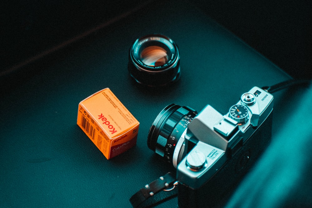 Obiettivo della fotocamera argento e nero accanto alla scatola arancione e bianca