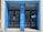 The entrance features two black glass doors framed by a blue facade. Text in white on the blue background reads 'Bibliothèque Quentin Blake' and 'Institut Français'. There are notices posted on the glass doors, and reflections can be seen in the glass.