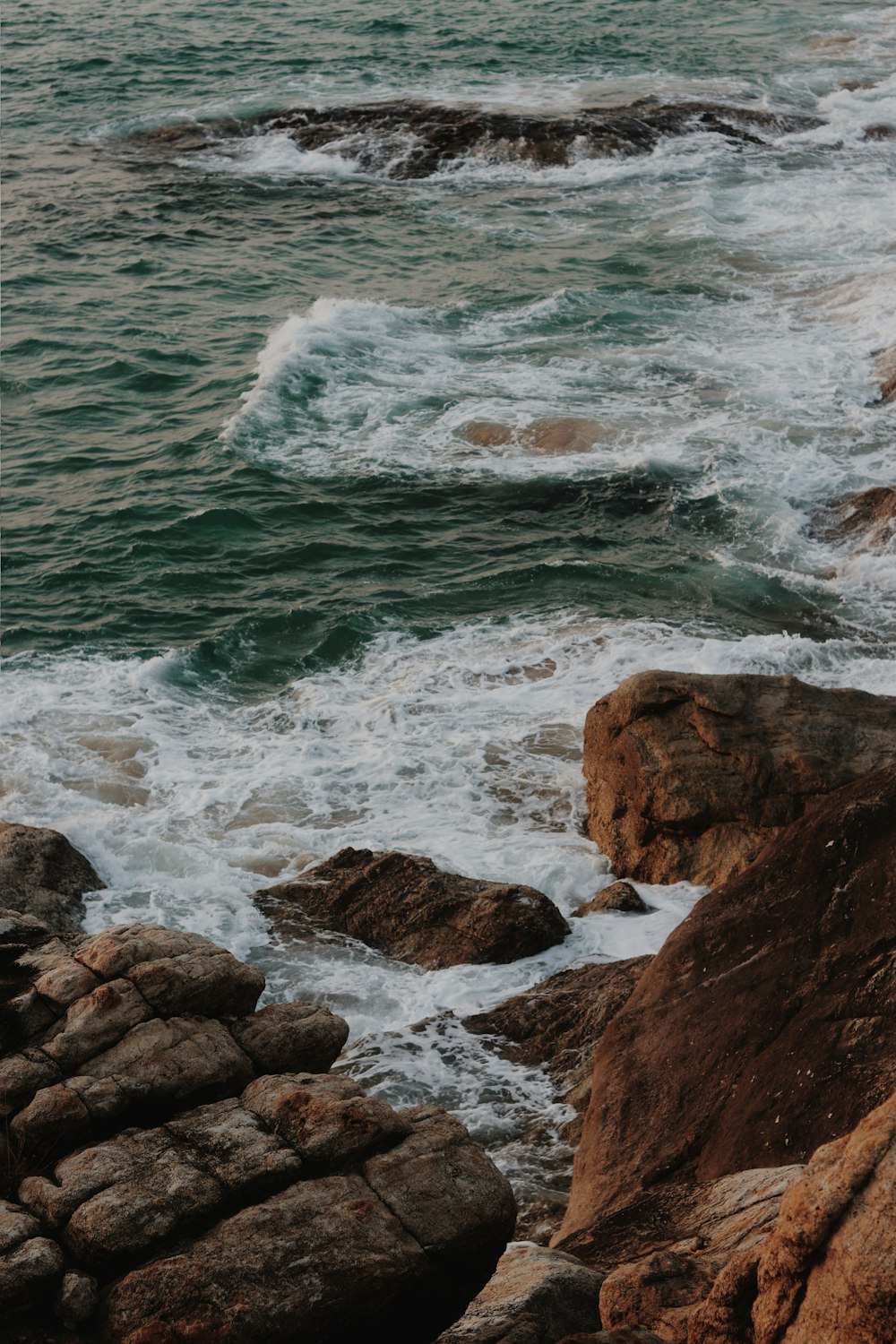 brown rocky shore with ocean waves crashing on rocks during daytime