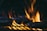 Hamburger patties being grilled with bright flames rising between them, emphasizing the high heat and intensity of the cooking process.
