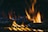 Hamburger patties being grilled with bright flames rising between them, emphasizing the high heat and intensity of the cooking process.
