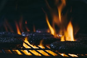 Slow-motion shot of a burger patty hitting the grill with flames rising around it