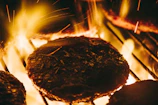 Top-down shot of a sizzling hamburger patty cooking on a grill with flames in the background.