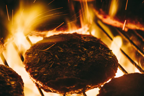 Close-up of a juicy grilled burger sizzling over hot charcoal flames.