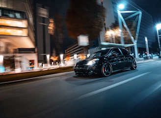 A sleek black sports car speeding through a neon-lit city street at night.