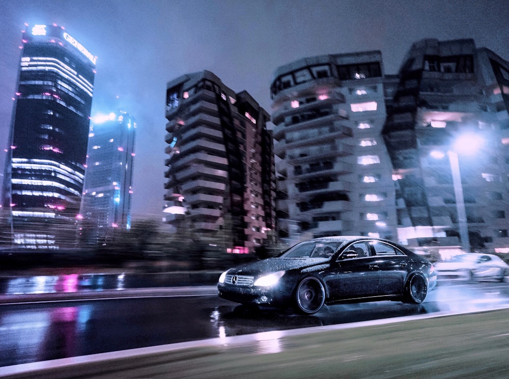 black sedan on road near high rise buildings during night time