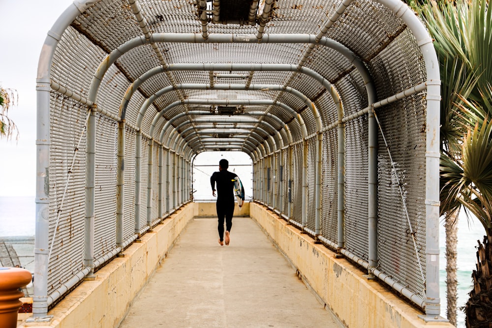 Hombre con camisa negra caminando sobre un puente de concreto marrón durante el día