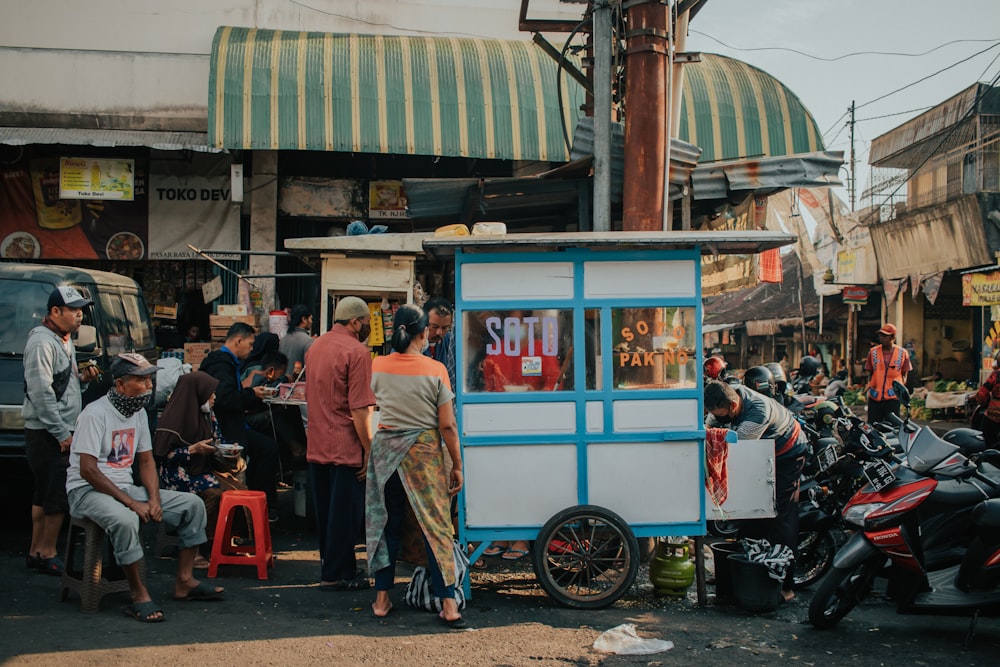 personnes debout près d’un stand de nourriture bleu et blanc pendant la journée