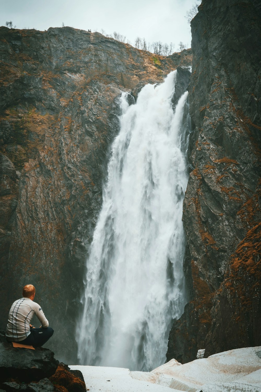 man in white shirt standing in front of waterfalls during daytime