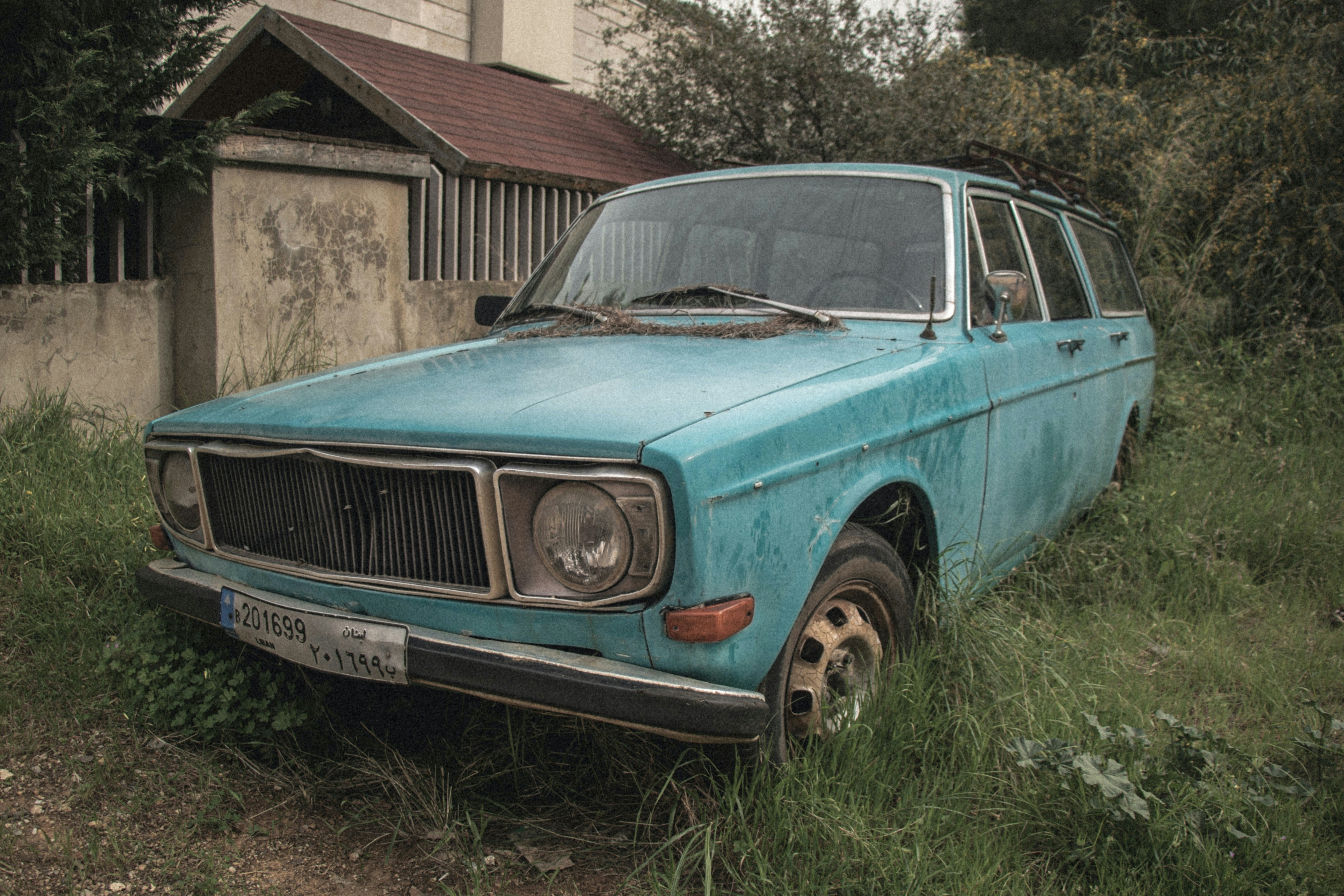 teal classic car parked beside brown concrete building during daytime