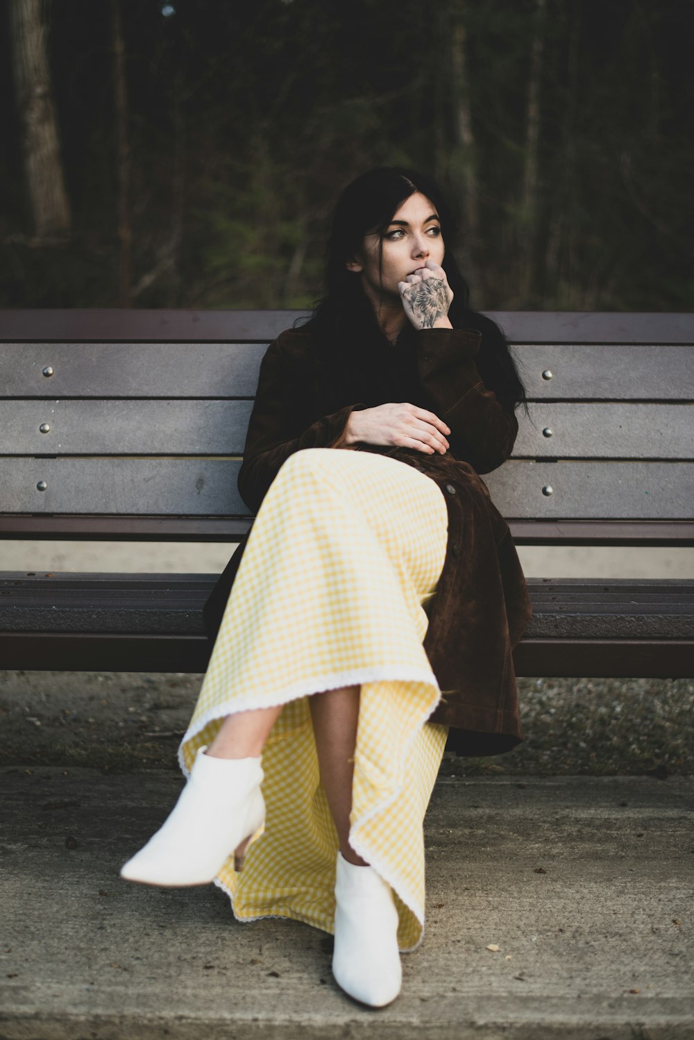 woman in black coat and white skirt sitting on brown wooden bench