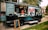 A food truck parked on a paved walkway surrounded by green grass. The truck has a large logo 'Marty's' on its side and is decorated with city skyline graphics. The serving window is open, with two staff members visible inside, and a vertical menu board stands in front. Several coolers are placed on the ground nearby.