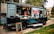 A food truck parked on a paved walkway surrounded by green grass. The truck has a large logo 'Marty's' on its side and is decorated with city skyline graphics. The serving window is open, with two staff members visible inside, and a vertical menu board stands in front. Several coolers are placed on the ground nearby.