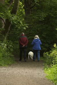 man and woman with white dog walking on dirt road during daytime