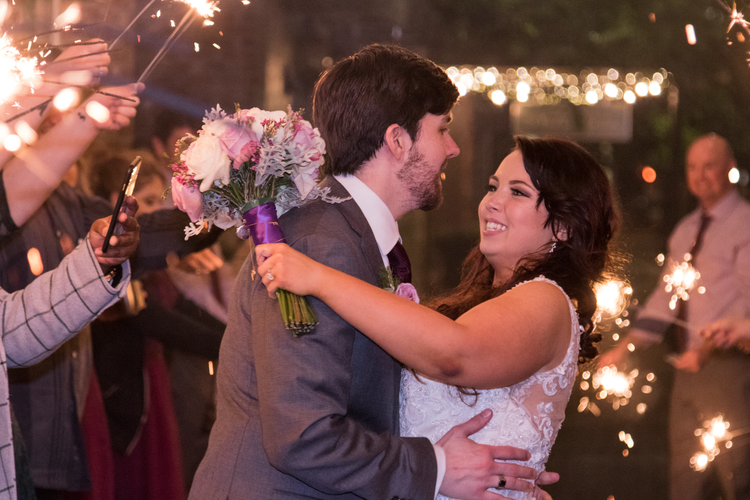 A couple laughing as guests wave sparklers around them