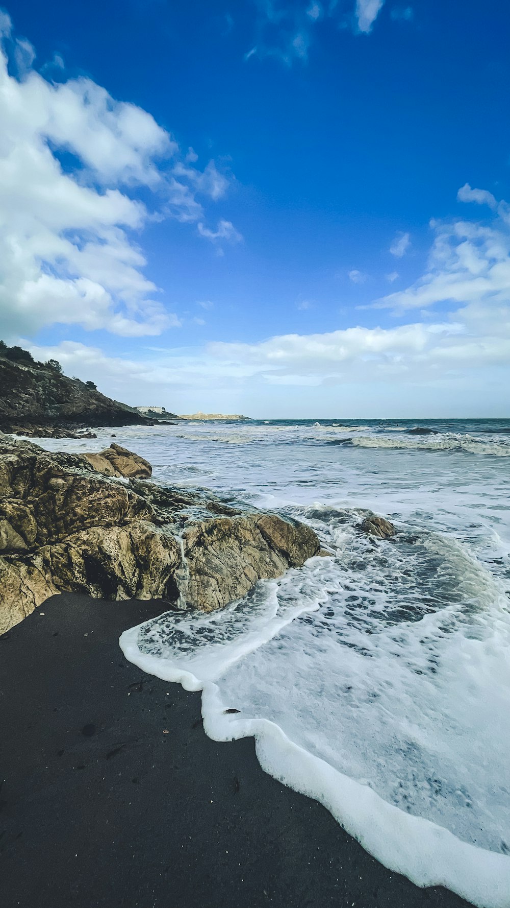 ocean waves crashing on rocky shore under blue and white cloudy sky during daytime