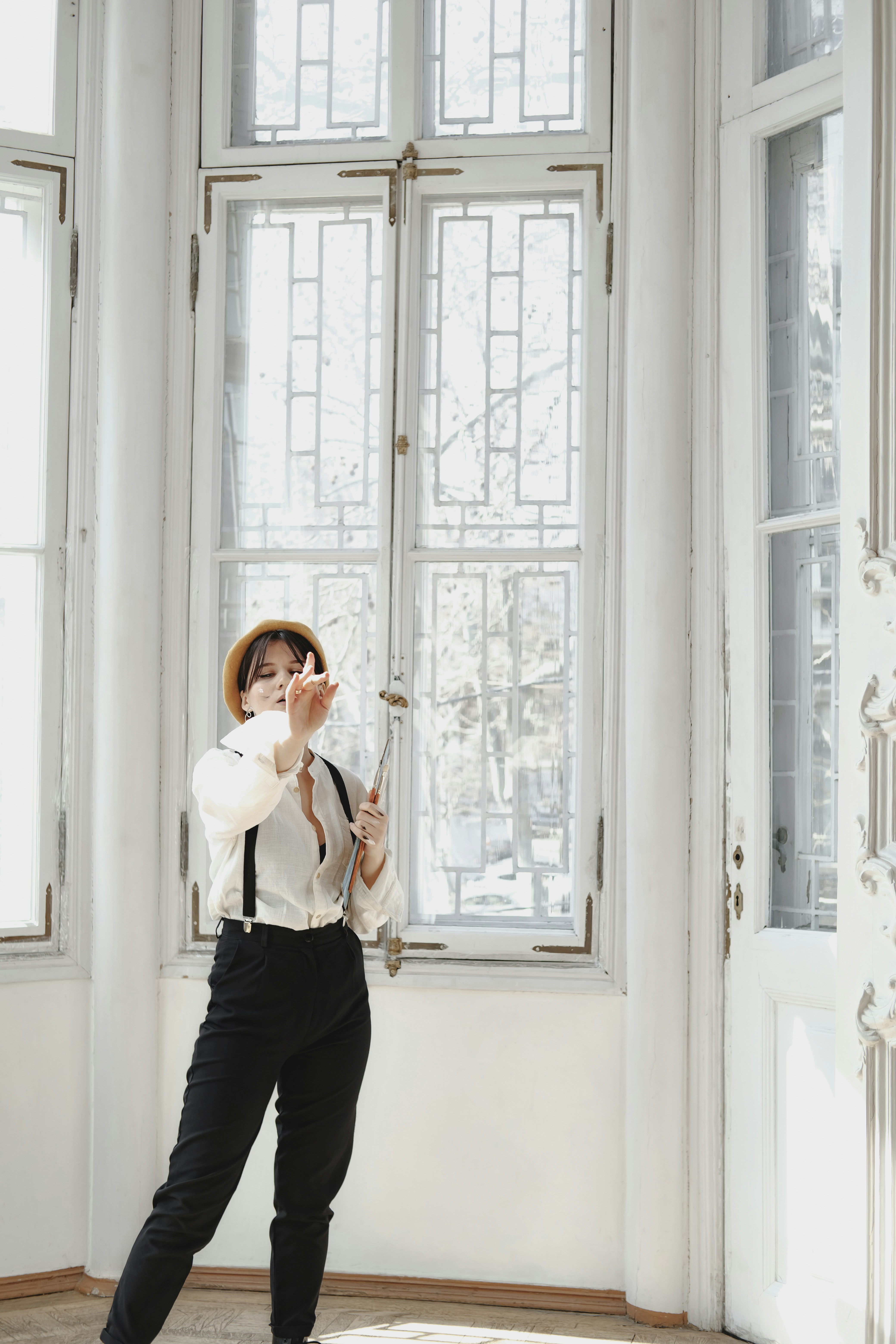 woman in white long sleeve shirt and black pants standing beside white wooden window