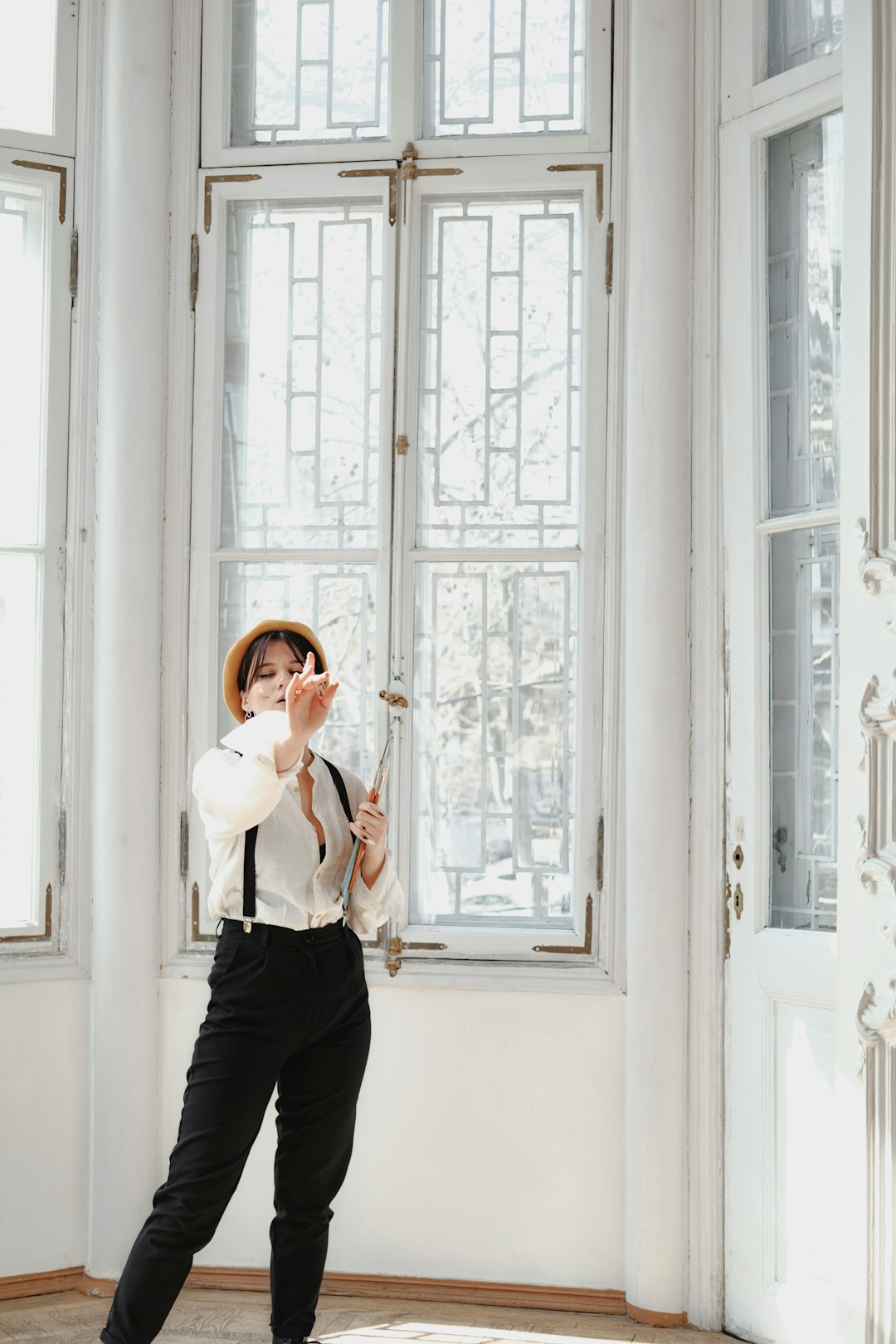 woman in white long sleeve shirt and black pants standing beside white wooden window