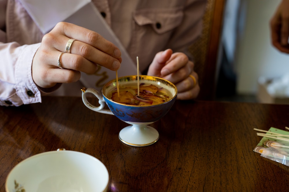 Persona che tiene il cucchiaio d'argento sulla tazza da tè in ceramica bianca