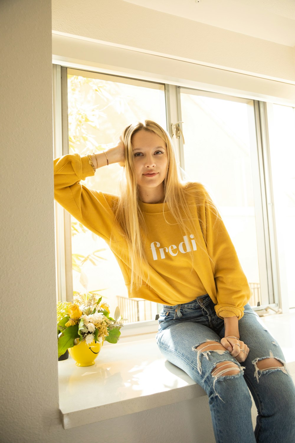 woman in yellow long sleeve shirt and blue denim jeans sitting on window during daytime