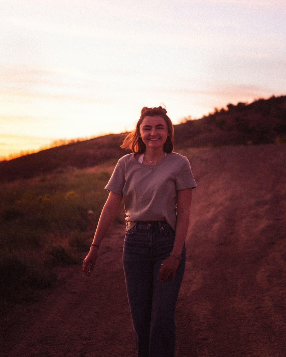 woman in gray crew neck t-shirt and blue denim jeans standing on brown dirt road