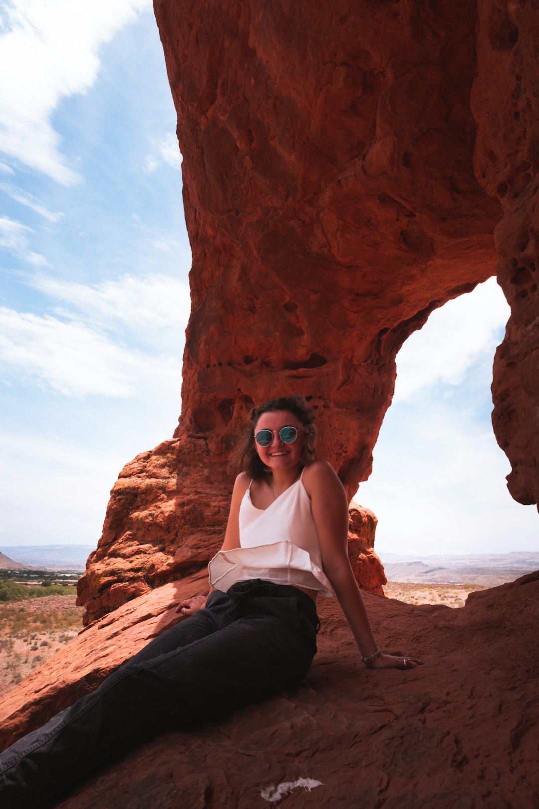 woman in white tank top and black pants sitting on brown rock formation during daytime