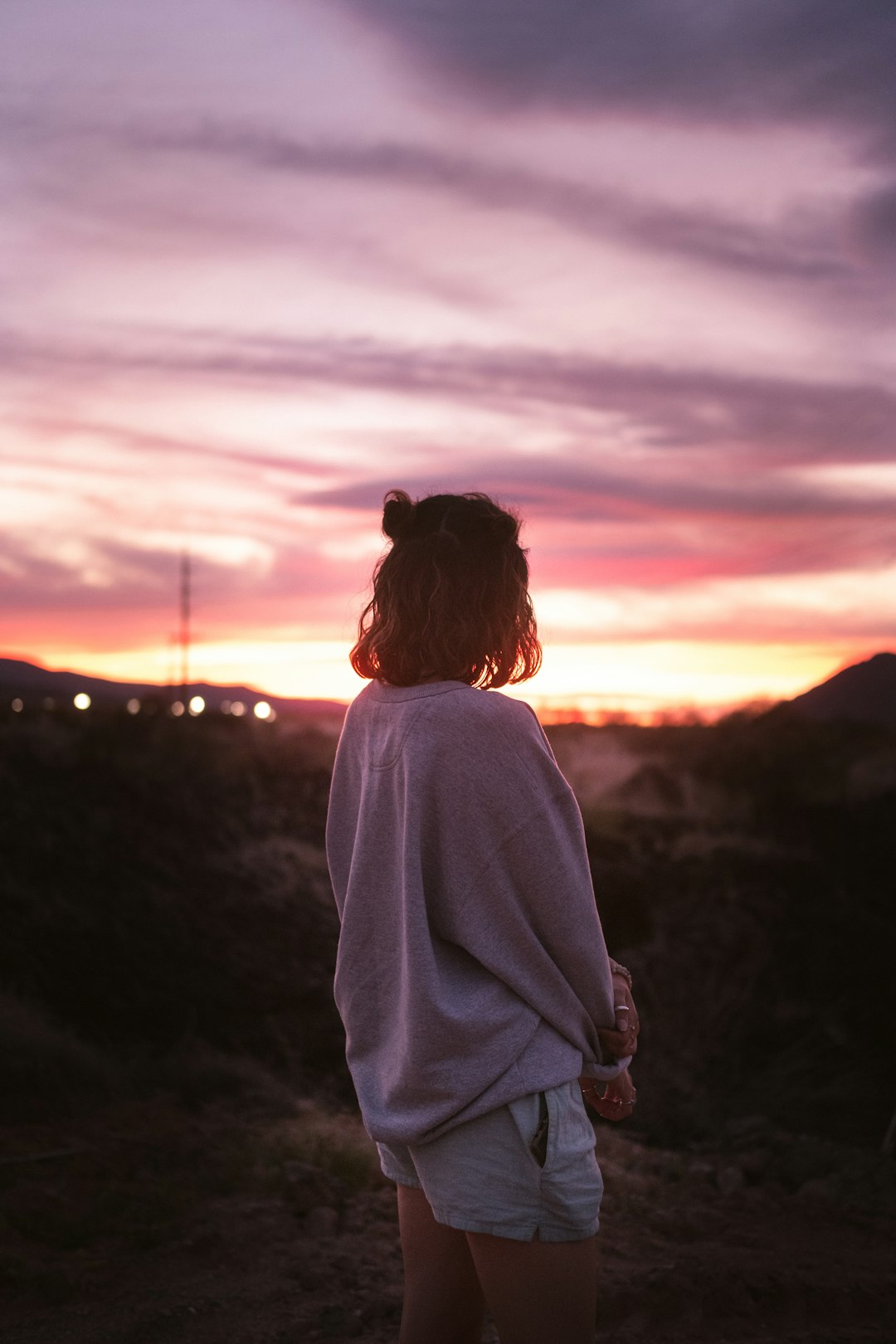 woman in white long sleeve shirt standing on hill during sunset