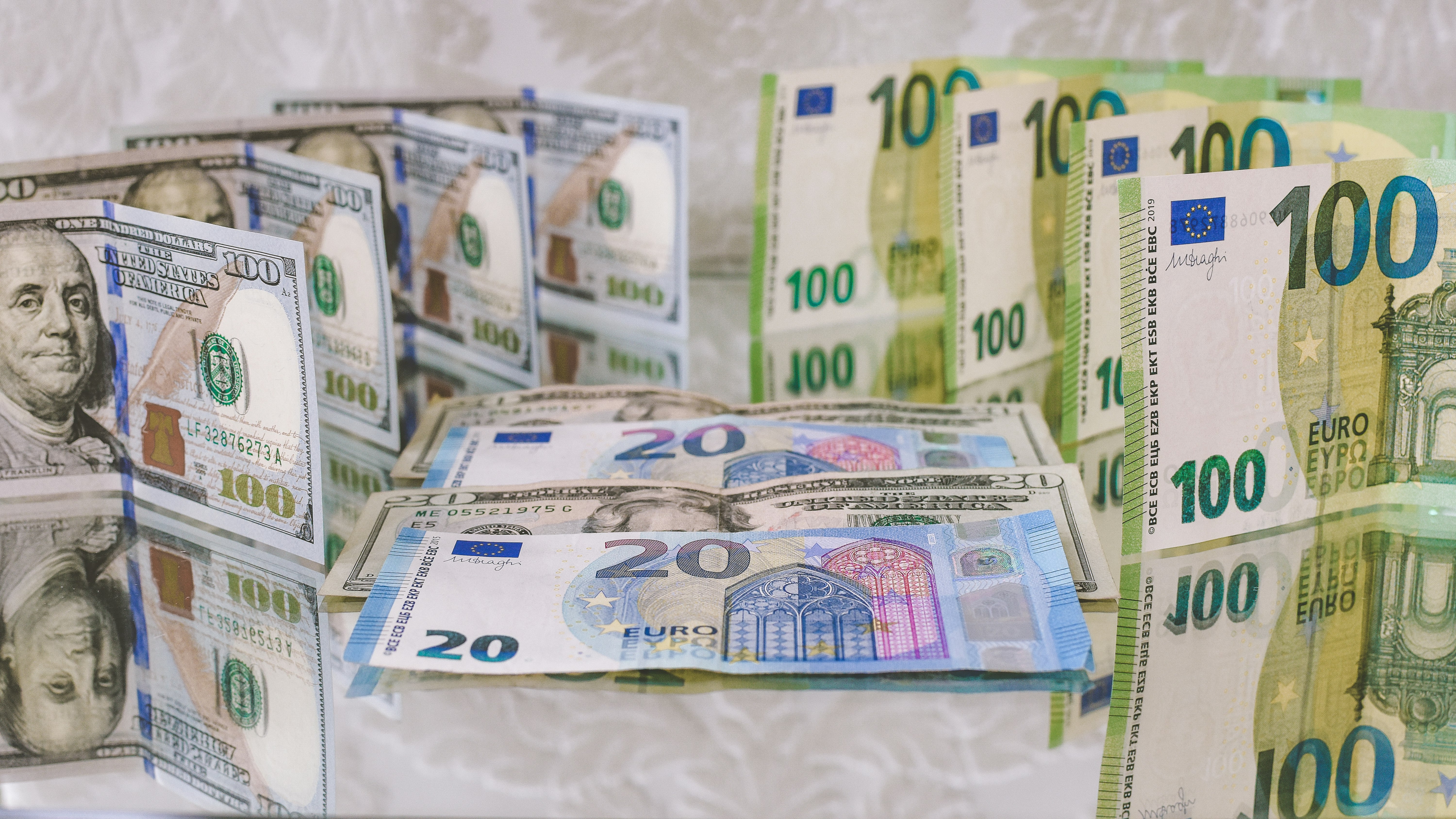 100, 20 Euro (EUR), and 100, 20 Dollar (USD) banknotes placed back-to-back vertically and horizontally on a reflecting surface.
