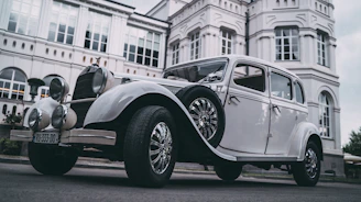 A vintage European-style classic car parked in front of an elegant mid-century modern building