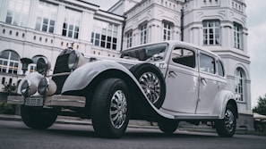 A beautifully restored electric car in front of a historic hotel entrance.